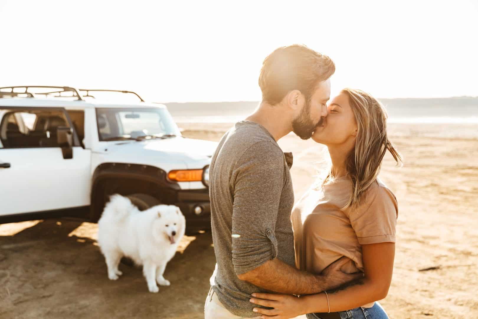 Young couple kissing on beach honeymoon with pet dog sitting by white jeep